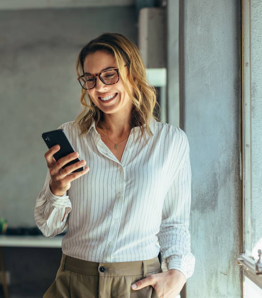 Stojąca kobieta z uśmiechem wpatrzona w telefon